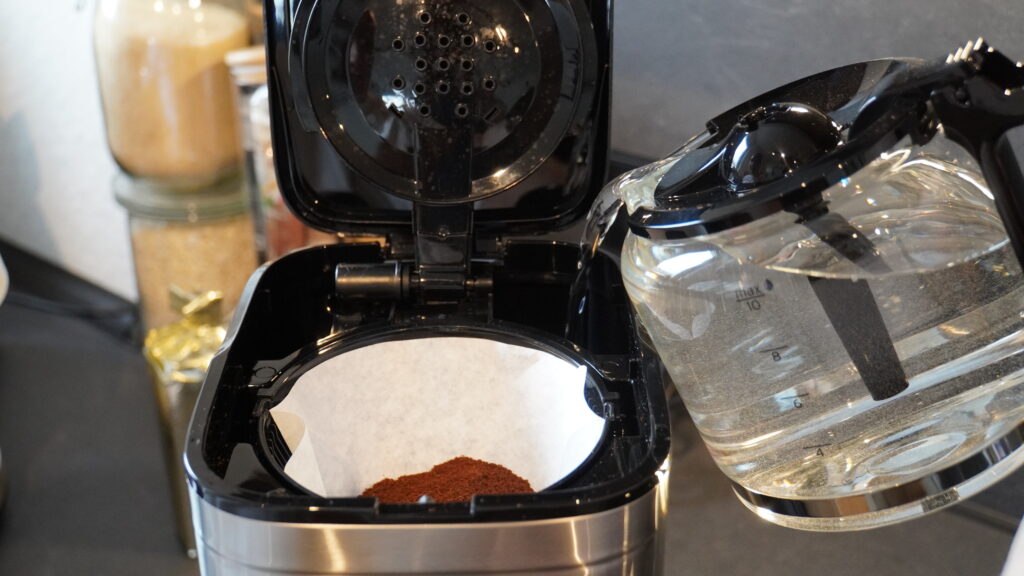 Kaffeemaschine mit einem Filtereinsatz, in den Wasser gegossen wird, während gemahlener Kaffee sichtbar ist.