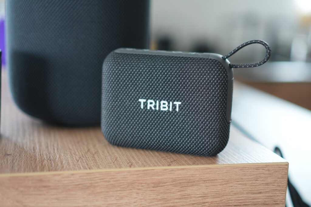 Kompakter schwarzer Tribit PocketGo Bluetooth-Lautsprecher mit Stoffoberfläche und Tribit-Logo auf einem Holztisch; kompakt, robust und ideal für den Alltag.