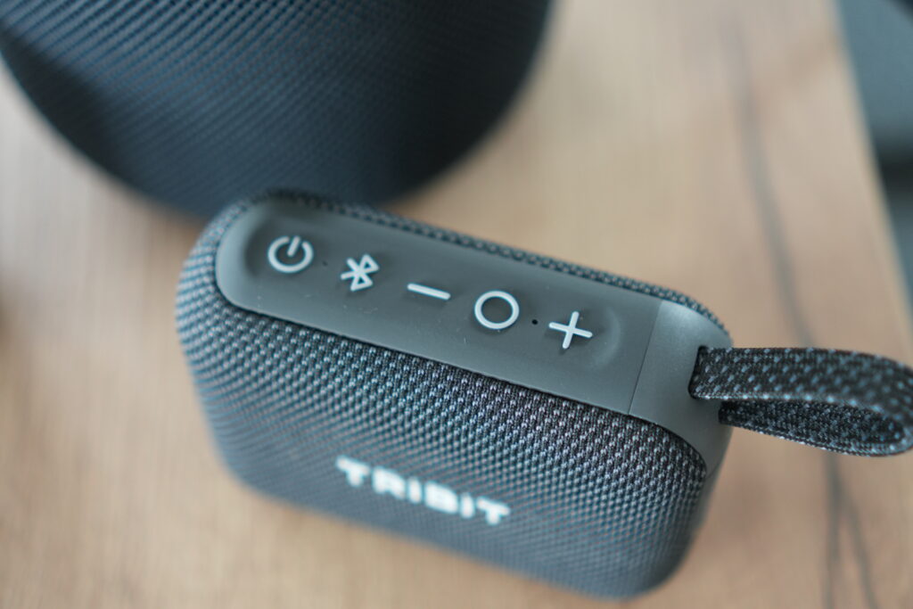 Nahaufnahme des Tribit PocketGo Bluetooth-Lautsprechers mit Power- und Bluetooth-Tasten, kompakte Stoffverarbeitung, IP68-Wasserdichtheit sichtbar