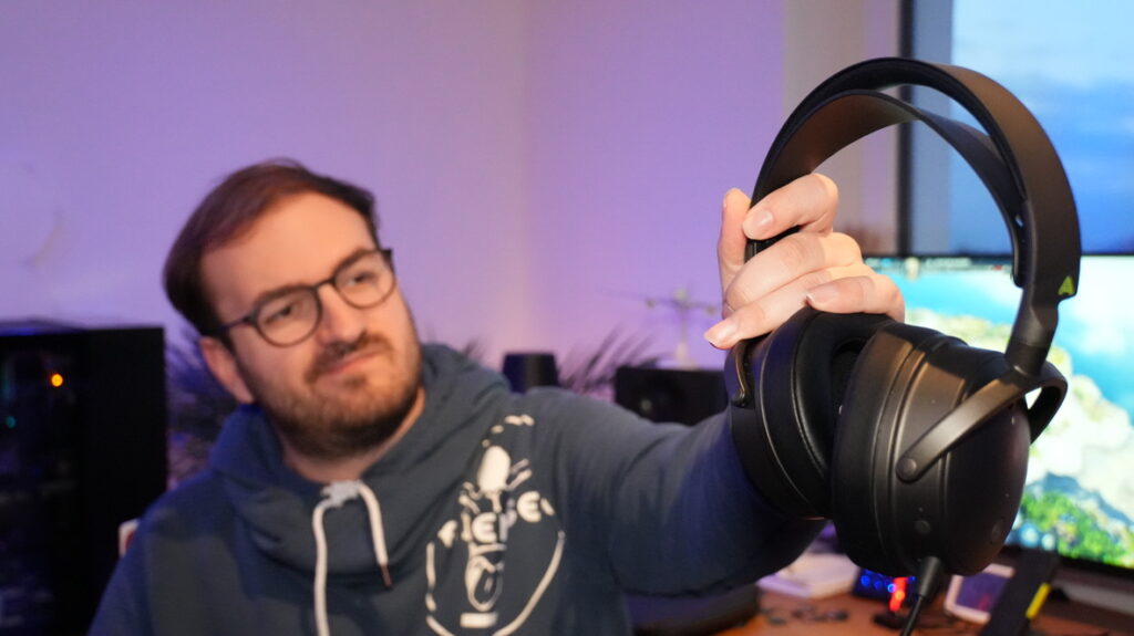 Audeze Maxwell Gaming-Headset in schwarz, großes Over-Ear Kopfhörer-Design, gehalten von einer Person mit Brille