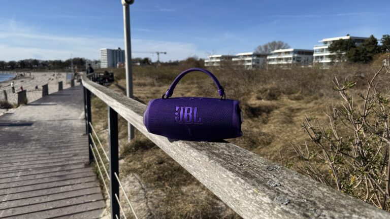 Lila JBL Charge 6 Bluetooth-Lautsprecher mit Tragegriff und JBL-Logo, mit Textilgewebe und robusten Gummi-Schutzbereichen im Außenbereich.