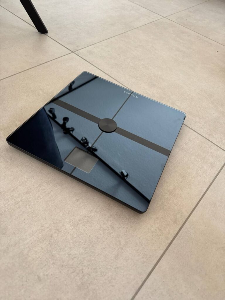 Die Withings Body Smart mit blauem Farbdisplay auf Fliesen: digitale Waage für Gewicht und Körperfett – nachweislich klinisch geprüft.