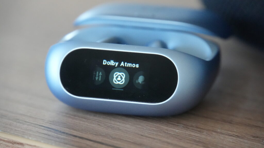 Auf dem Display der Soundcore Liberty 5 Pro von Anker ist Dolby Atmos zu sehen, während die blaue Ladehülle mit den Ohrhörern daneben liegt.