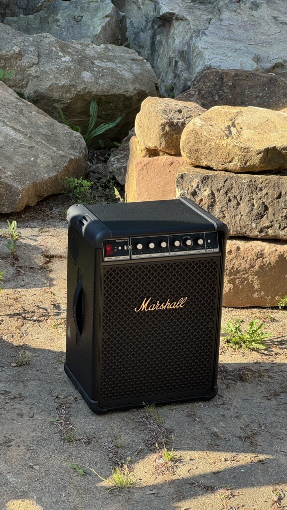 Schwarzer Marshall Bromley 450 Party-Lautsprecher mit goldener Frontschrift und Reglern steht im Freien auf sandigem Boden zwischen großen Felsen.