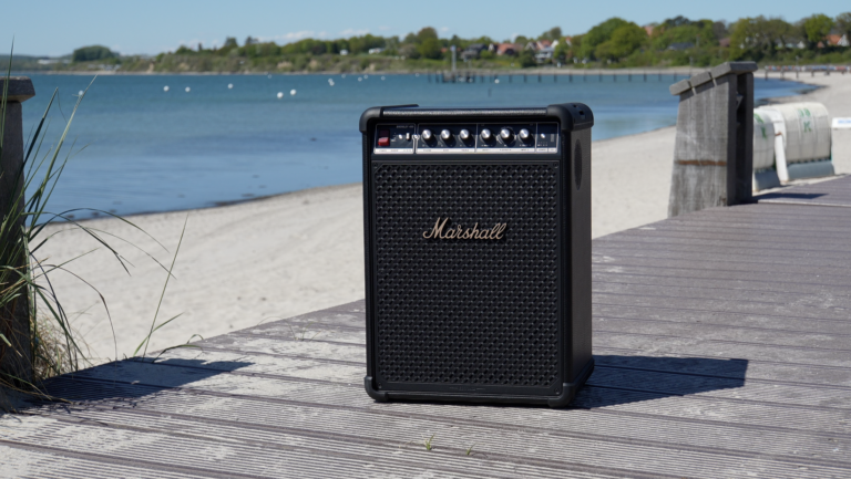 Am Strand steht der schwarze Marshall Bromley 450 mit goldenen Akzenten auf einem Holzsteg und zeigt sein klassisches Amp-Design.