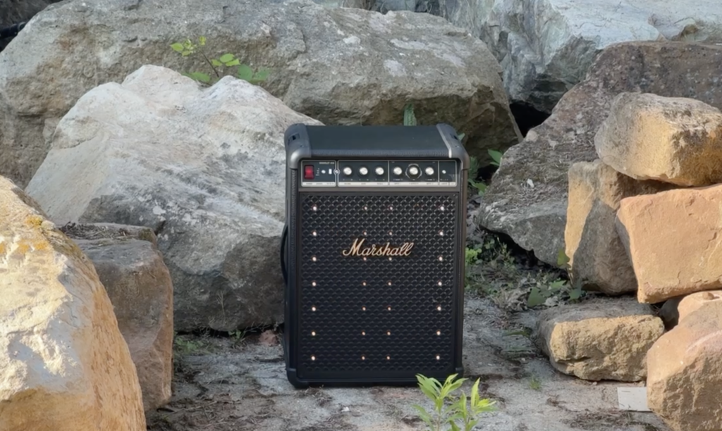 Vor grauen Felsen steht der Marshall Bromley 450 mit schwarzem Gehäuse, goldenen Details und dezenten LED-Punkten auf der Front im Garten.