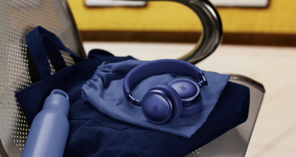 Blaue JBL Live Kopfhörer mit gepolsterten Ohrmuscheln auf einem weichen Tuch im Reise-Setup, klar erkennbares JBL-Logo.