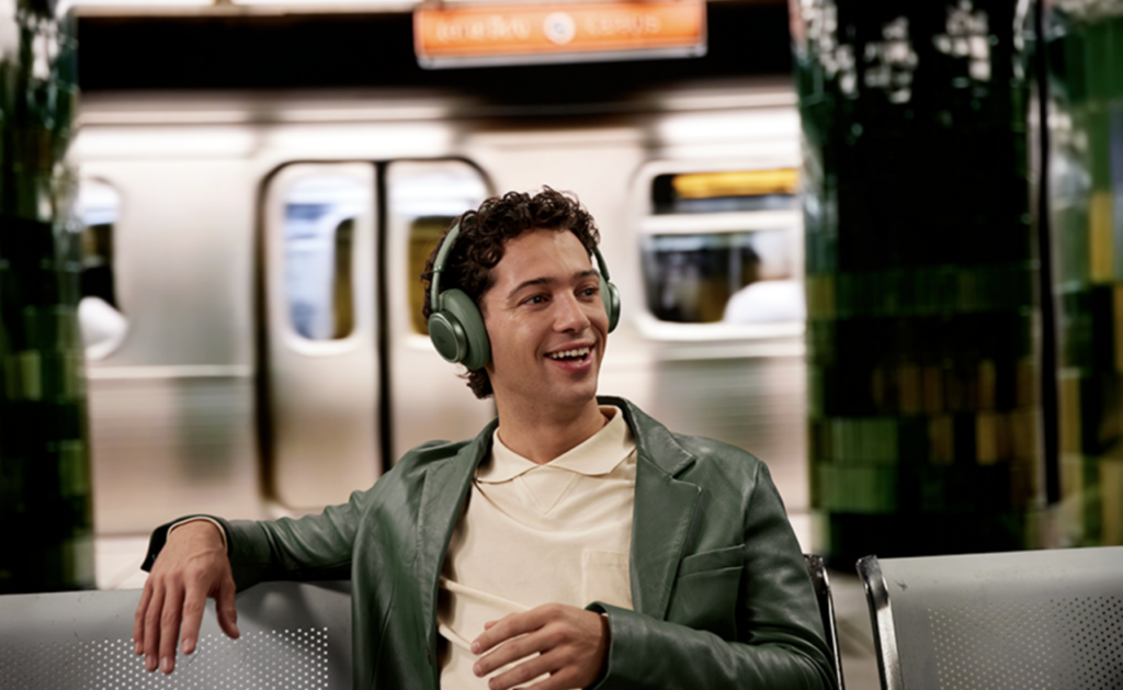 JBL Live 780NC in Grün: Over-Ear-Kopfhörer an einem Mann in der Bahn, entspanntes Zuhören, während das Noise Cancelling im Hintergrund wirkt.