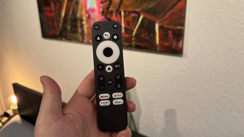 Eine Hand hält die Fernbedienung des Wanbo Cube 2 Pro, des kompakten Full-HD-Beamers mit Android TV und Schnellzugriff auf YouTube, Netflix und Prime Video.