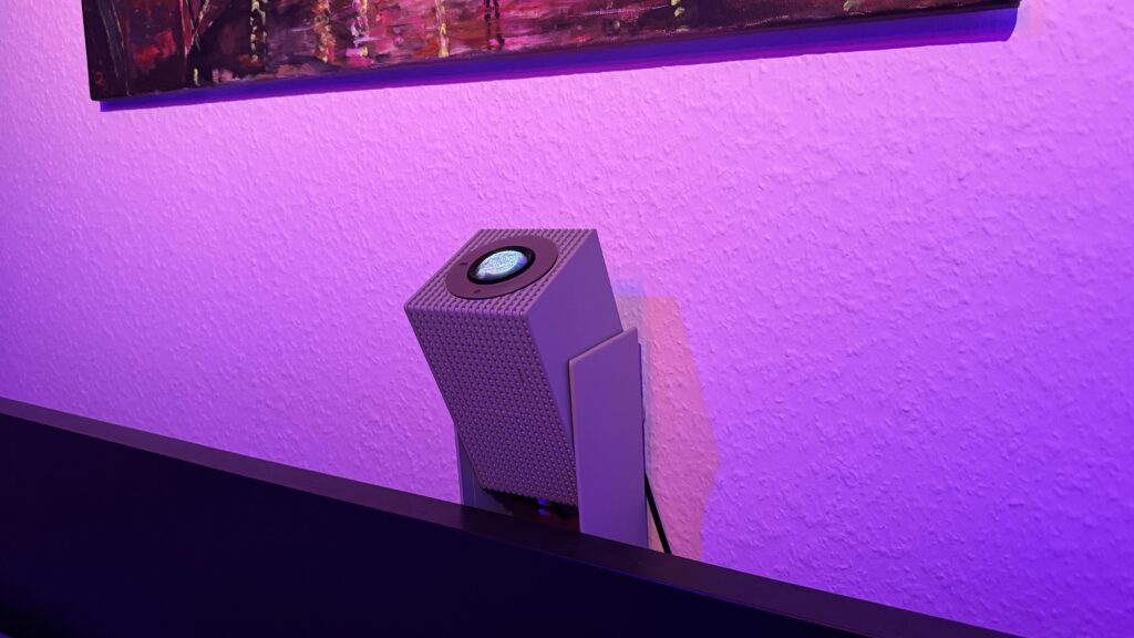 In einem abgedunkelten Raum steht der Wanbo Cube 2 Pro mit gekipptem Gimbal-Standfuß vor einer violett beleuchteten Wand.