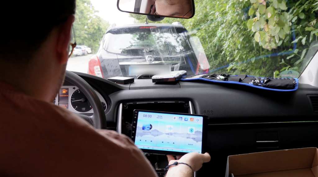 Im Innenraum einer Mercedes B-Klasse sitzt ein Mann vor einem ausgebauten Armaturenbrett und testet ein Android-Autoradio mit CarPlay und Android Auto.