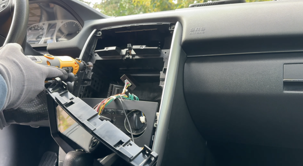 Im Armaturenbrett einer Mercedes B-Klasse wird ein Android-Autoradio mit Kabeln, Blende und Schrauber bei der Nachrüstung im alten Auto montiert.