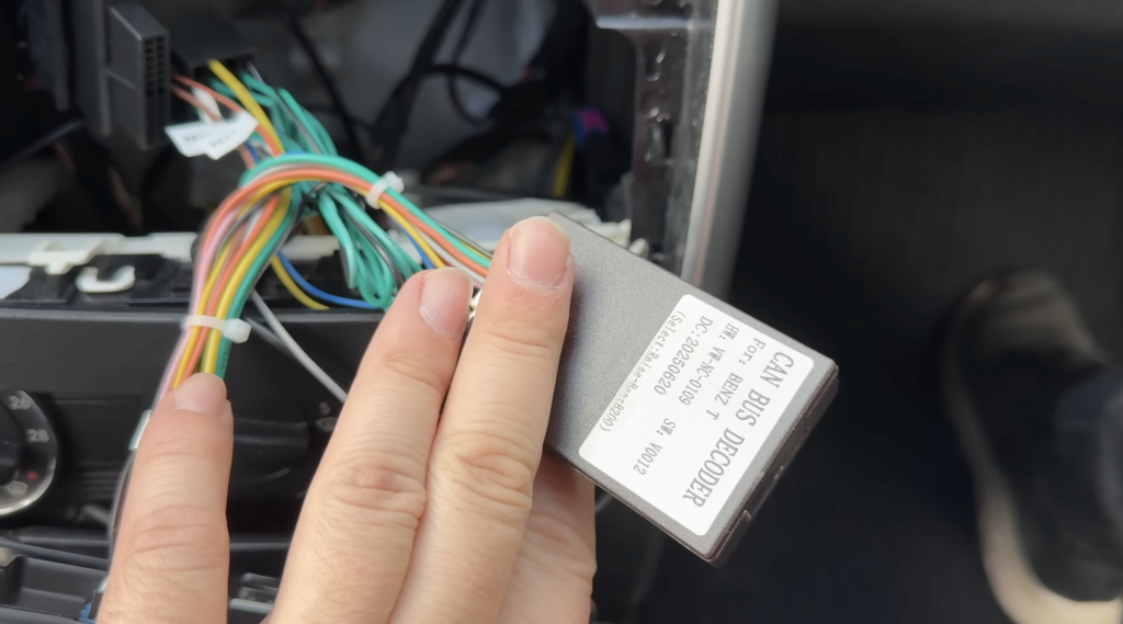 Ein CAN-Bus-Decoder mit bunten Kabeln wird in der Mittelkonsole einer Mercedes B-Klasse von 2010 an das Nachrüst-Autoradio angeschlossen.