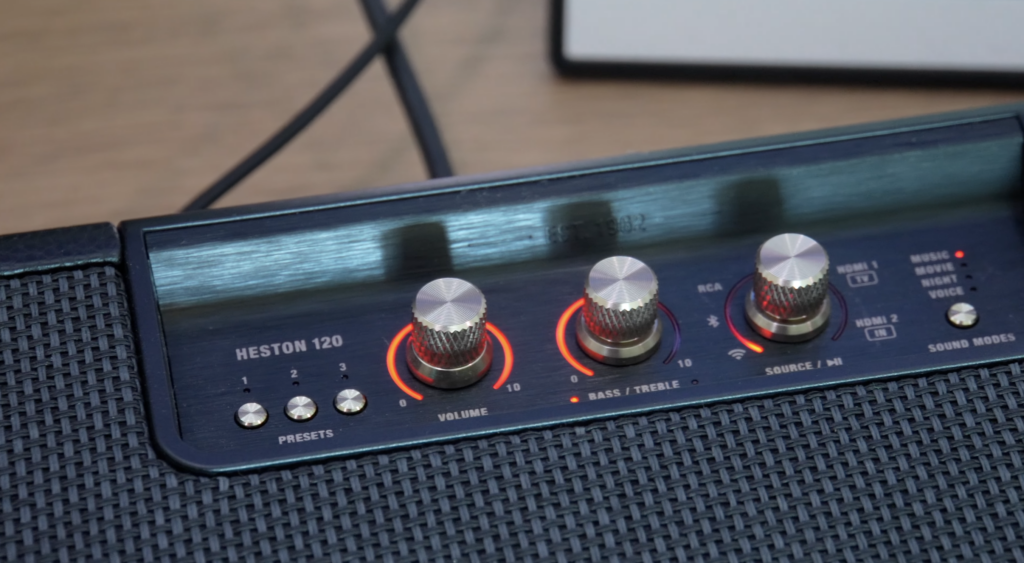 Auf der Marshall Heston 120 leuchten drei silberne Regler und Preset-Tasten, während die Bedienoberfläche für Bass, Treble und Quellen sichtbar ist.