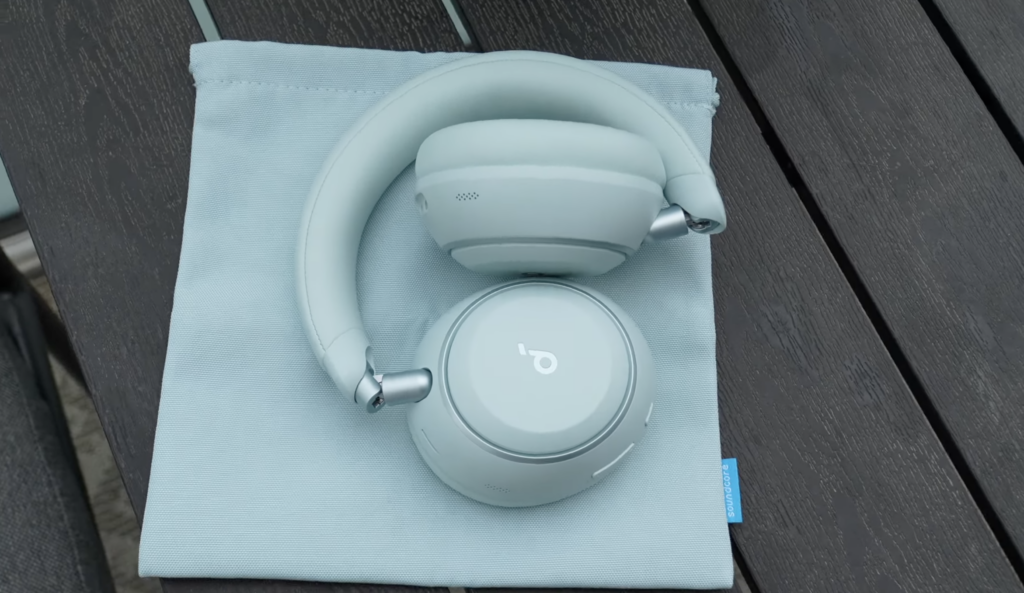 Die hellblauen Soundcore Space 2 Over-Ear-Kopfhörer liegen gefaltet auf einer Stofftasche, mit sichtbarem Soundcore-Logo und Scharnieren.