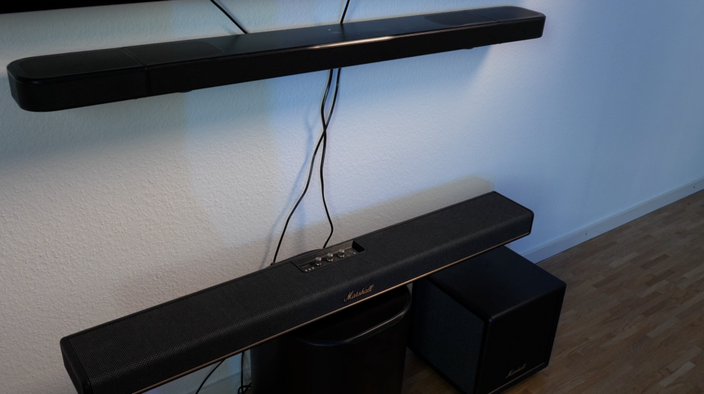 Eine schwarze Marshall Heston 120 hängt an der Wand, darunter steht der passende Subwoofer neben einer zweiten Soundbar im direkten Vergleich.
