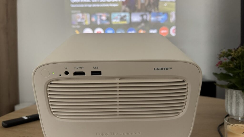 Der Wanbo Vali 1 Pro steht vor einer projizierten Google-TV-Oberfläche auf einem Tisch im Wohnzimmer.