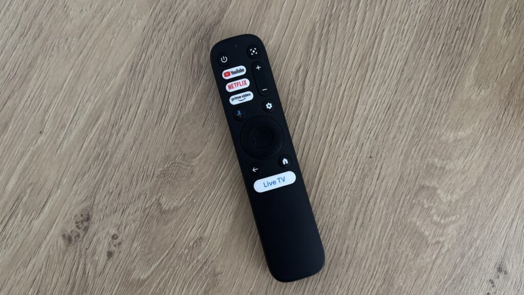 Schwarze Fernbedienung mit YouTube-, Netflix-, Prime-Video- und Live-TV-Tasten liegt auf einer Holzoberfläche.