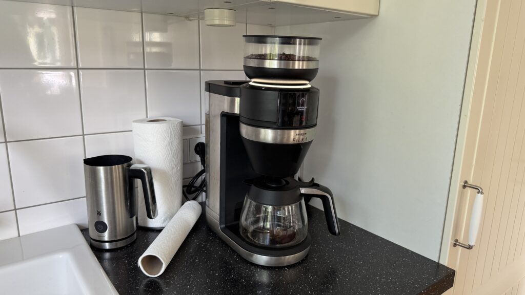 Die Severin Filka steht in einer Küche mit Bohnenbehälter, Glaskanne und Edelstahloberfläche neben Küchenpapier.