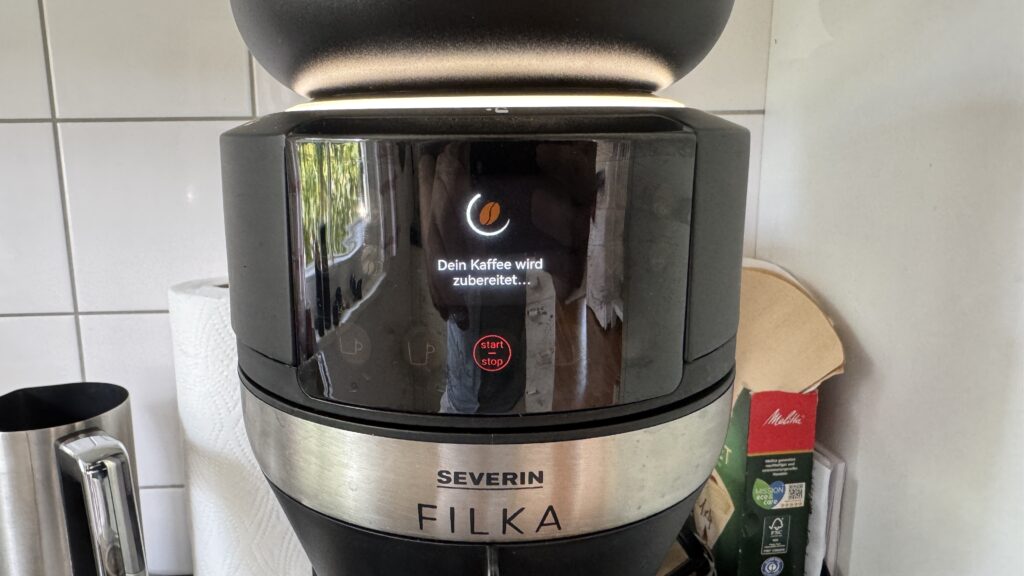 Die schwarze Severin Filka zeigt auf dem Display „Dein Kaffee wird zubereitet...“, während der Brühvorgang läuft.
