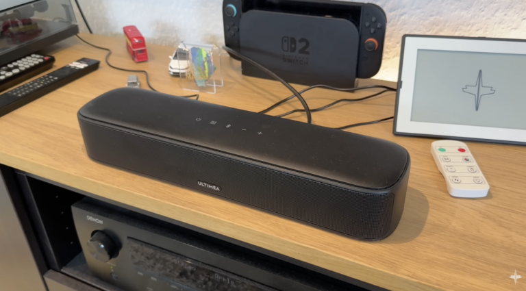 Die schwarze Ultimea Aura S4T steht auf einem Holzsideboard neben einer Fernbedienung und einem Nintendo Switch OLED-Dock.